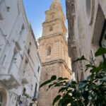 A narrow street with a church steeple in the background