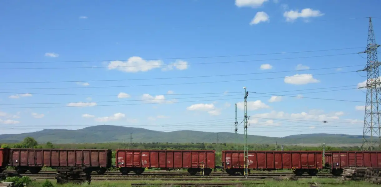 A red train traveling down train tracks next to a lush green field
